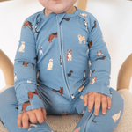 Child wearing a blue onesie with dog pattern sitting on a beige chair.