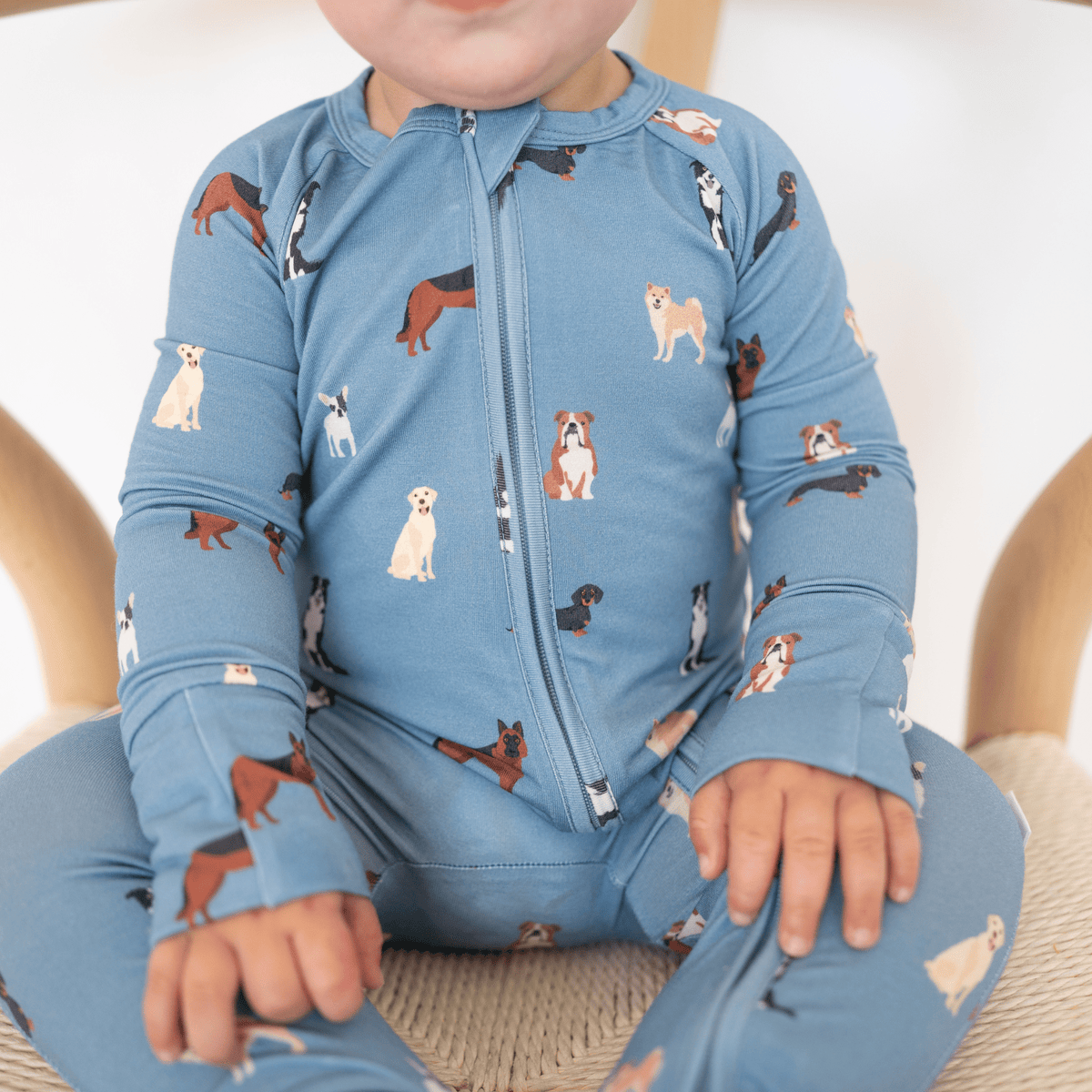 Child wearing a blue onesie with dog pattern sitting on a beige chair.