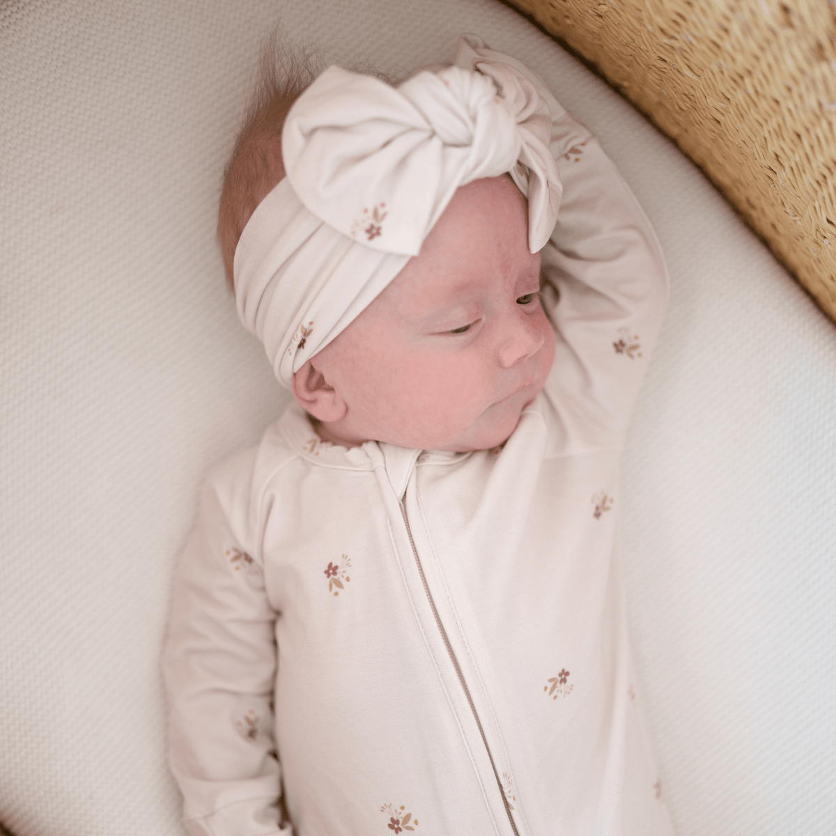 Newborn baby wearing a white headband and floral outfit on a neutral background