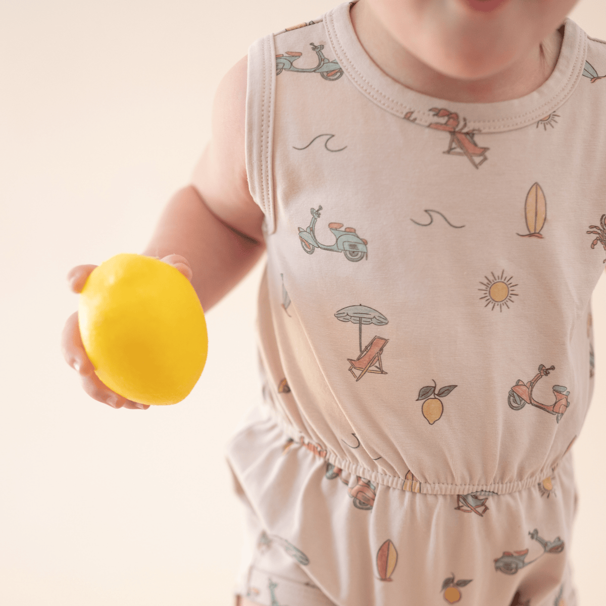 Baby girl in Summer Vibes romper holding lemon.