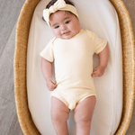 Smiling baby lying in a Moses basket wearing the organic cotton Lemonade Yellow bodysuit and matching headband from bug + bean kids