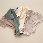 Overhead flat lay of bug + bean organic cotton baby bodysuit collection in neutral tones and Summer Vibes print