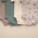 Flat lay of four organic cotton baby bodysuits including Summer Vibes and solids, highlighting bottom snap closures