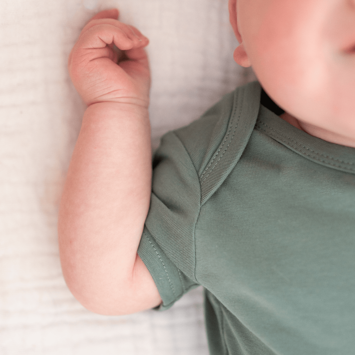 Detail shot of baby arm and sleeve seam of sage green organic cotton short sleeve bodysuit