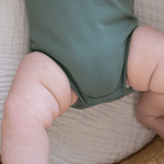 Close-up of snap buttons and chubby baby legs in sage green organic cotton bodysuit