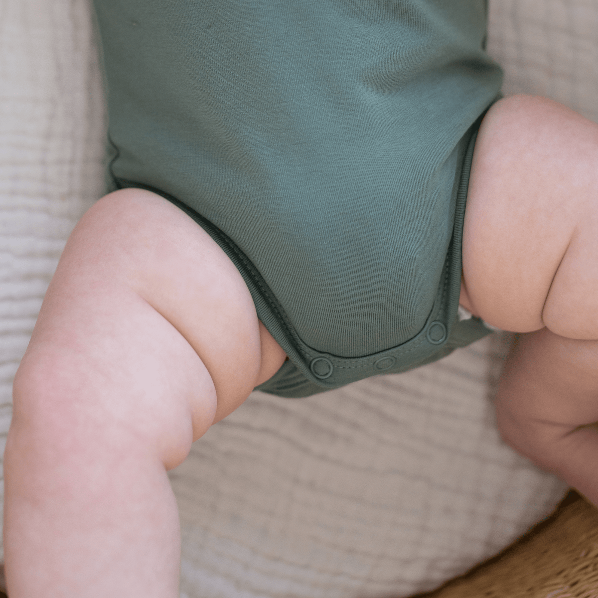 Close-up of snap buttons and chubby baby legs in sage green organic cotton bodysuit