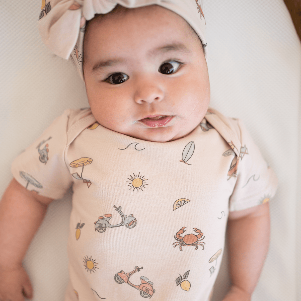 Close-up of baby girl wearing organic cotton Summer Vibes bodysuit featuring crabs, scooters, and lemons print
