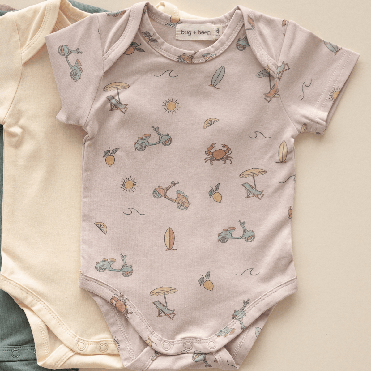 Flat lay of organic cotton Summer Vibes bodysuit with playful summer icons including scooters, umbrellas, and lemons