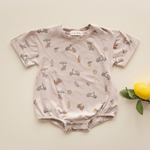Flat lay of bug + bean Summer Vibes bubble romper with playful beach print and lemon prop on cream background