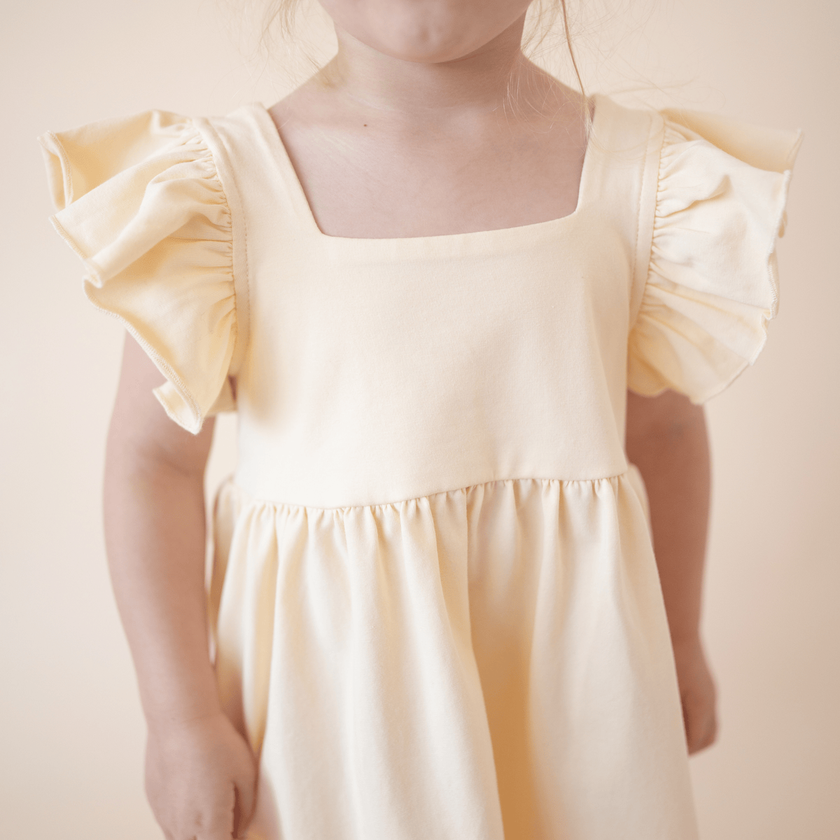 Close-up of the ruffled sleeve and square neckline on the bug + bean kids organic cotton lemonade yellow dress.
