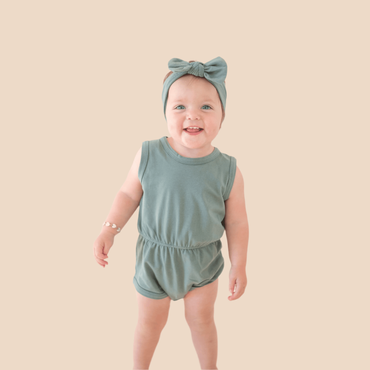 Baby girl in sage green romper with bow.