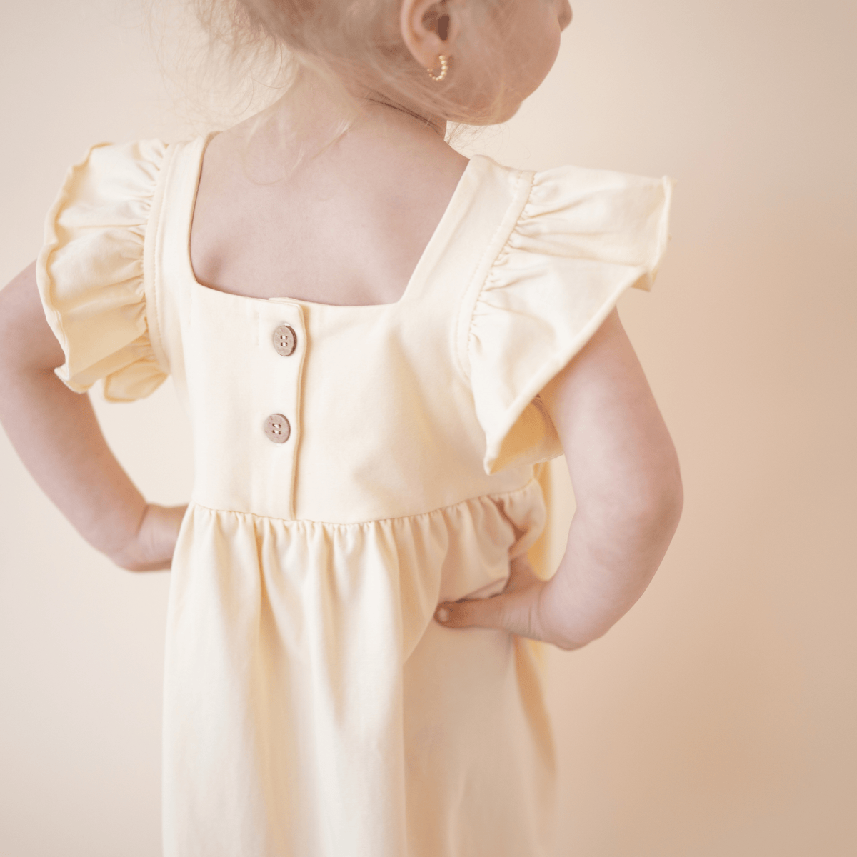 Back view of bug + bean kids organic cotton lemonade yellow dress featuring natural coconut button details.