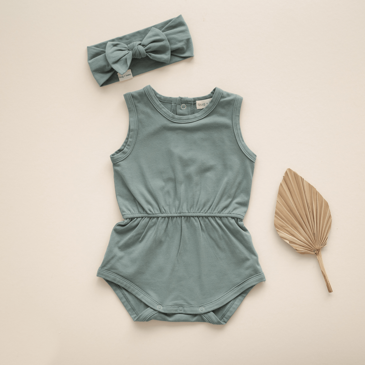 Green baby romper and bow headband flat lay.
