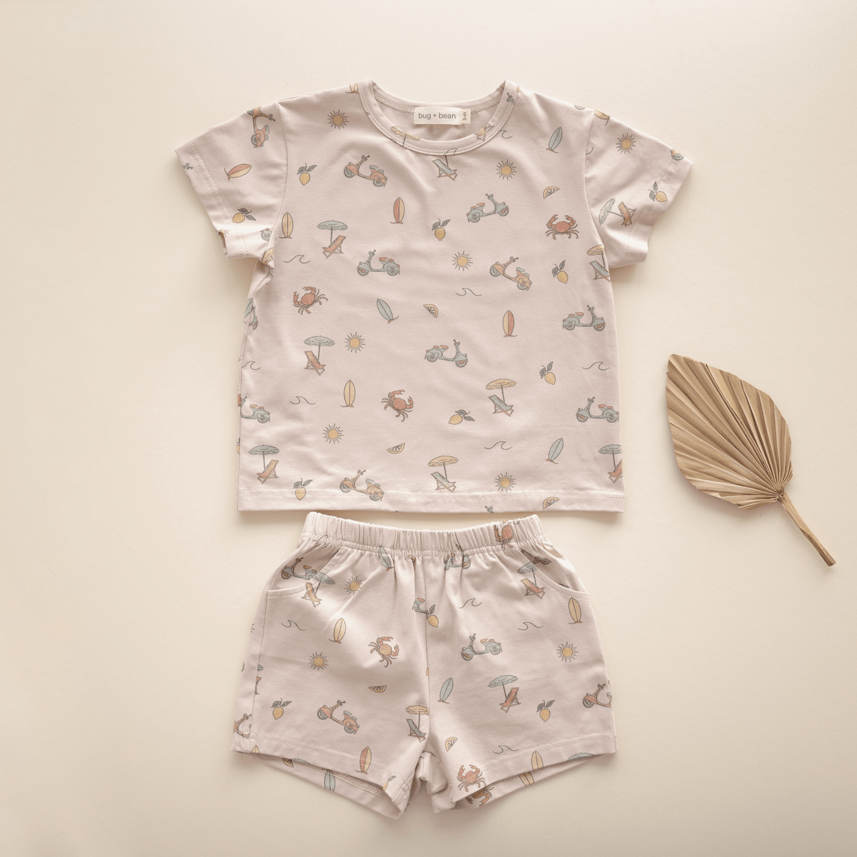 Flat lay of bug + bean kids Summer Vibes organic cotton short set for toddlers, featuring a whimsical beach-themed print on a soft neutral background.